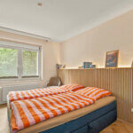 Schlafzimmer mit Doppelbett, Holzlamellenwand und Fenster zum Park