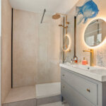 Modernes Badezimmer mit Glasdusche, Waschtisch und beleuchtetem Rundspiegel