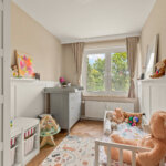Helles Kinderzimmer mit Kinderbett, Wickelkommode und Fenster ins Grüne
