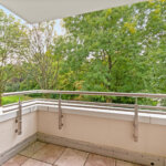 Überdachter Westbalkon mit Metallgeländer und Blick auf grüne Bäume